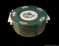 Stacked view of all 12 porcelain plates showing top plate with a bird design and turquoise with gold rim.