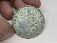 Obverse side of 1921 Morgan silver dollar held between fingers showing Lady Liberty profile and 'E PLURIBUS UNUM' inscription with the year 1921 beneath.