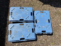 Three blue plastic furniture moving dollies stacked on the ground showing top surfaces with circular patterns and carry handles.