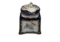 Front view of the antique porcelain jar showing hand-painted floral designs framed in gold on a dark blue background with sculpted floral lid handle.