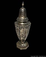Full view of the antique sterling sugar shaker with floral engraving and perforated top with finial.