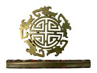 Bronze trivet with detailed Chinese design motifs centered above a wooden ruler for size comparison