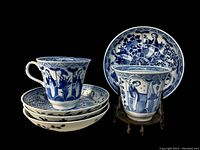 Two hand painted blue and white Chinese porcelain cups with four matching saucers stacked. Cups feature female figures and floral designs. Saucers underneath cups showing size and pattern.