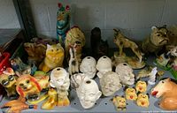 Shelf display of various chalkware figurines including dog breeds, human heads with hollow centers, a yellow cat, a Native American headdress figure, and other mixed animal shapes.