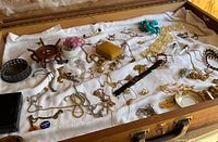 Overview of the jewelry lot laid on white cloth in an open wooden tray. Includes various jewelry pieces, accessories and badges.
