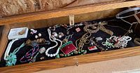 Full overview of jewelry items arranged in wooden tray with black fabric.