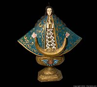 Front view of the painted wooden Madonna statue showing detailed patterns on robe, gold crescent base with cherub face, blue cloak with gold scrollwork and pink roses