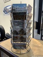 Front view of metal postcard rack with multiple vintage postcards including ferry boat, landscapes, and buildings.