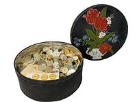 Photo of open black metal tin with decorative floral lid, shows a large quantity of assorted antique buttons inside.