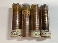 Four cylindrical rolls of 1963 wheat pennies with labels indicating uncirculated and circulated status and mint marks P and D