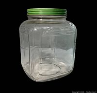 Front side view of the clear square glass jar with embossed sides and green metal screw lid.