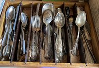 Top view of assorted vintage spoons, forks, and serving utensils arranged in wooden tray with dividers.