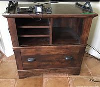 Front view showing multiple shelves on upper part and large filing drawer with metal cup handles beneath. Cabinet holds media and files.