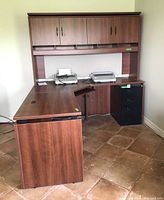 Corner office desk with hutch from an angle showing desktop, pull-out keyboard tray, and black filing cabinet.