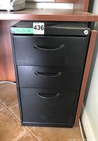 Front view of black metal file cabinet with three drawers and lock on top right corner.