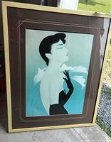 Framed print showing stylized portrait of woman in black gloves with blue background and decorative white detail. Frame is light gold and print is matted brown with gold bordering.