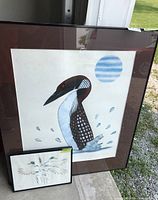 Two signed framed bird prints shown outdoors against a wall, the large print depicts a loon and the small print shows mallard ducks in flight.