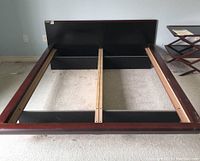 Full assembled wooden queen size bed frame viewed from the foot end, showing dark finished wood sides and black flat headboard panel.