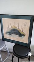 Framed Inuit style artwork depicting a turtle with sun and trees, matted and framed behind glass on a black frame.