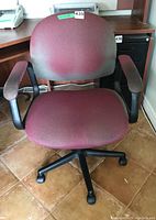 Front view of burgundy office chair showing seat, backrest, armrests, and five-wheel base on tiled floor.