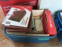 Blue plastic tote with assorted office supplies including red Basics brand file folder box, brown accordion file folders, beige hanging folders, and other office materials.