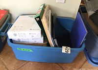 Blue tote filled with printer paper reams, file folders, ledger books, clipboard, and binder.
