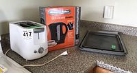 Photo showing Black & Decker toaster, Proctor Silex kettle box, and three cookie sheet pans on countertop.