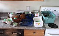 Full view of teapots, bowls, tray, strainer, candles and organizers arranged on kitchen counter.