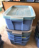 Four stacked plastic storage totes with lids, in shades of blue, showing some wear and dirt marks.