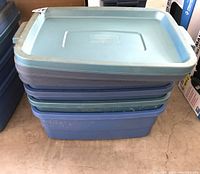Stack of four plastic storage totes with lids in blue and green colors, showing size and condition