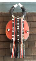 Front view of carved mask showing horns and painted stripe pattern