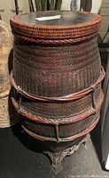 Full view of the round woven wicker basket with removable wooden lid and a decorative metal stand.