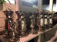 Seven mercury glass candle holders arranged on a white surface, varying sizes and styles visible.