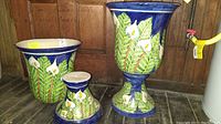 Pair of ceramic urns with floral and leaf decoration on blue background, one urn standing upright, other lying on side showing removable top and interior
