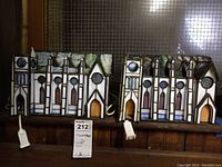 Pair of stained glass church panels with lighted electric cords for illumination, placed on a wooden surface in front of a metal mesh back.
