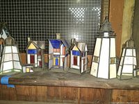 Overview of all eight stained glass cottage light houses on a wooden shelf with wire mesh background