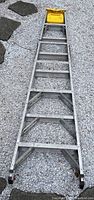 Full length photo of the 8ft aluminum ladder laid on gravel, showing overall weathered condition.