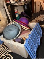 Plastic container filled with multiple ladies hats of varying colors and styles in a storage area.