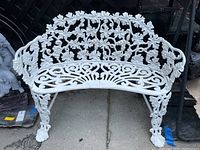 Front side view of the white floral design metal bench seating, showing ornate patterns and support legs.