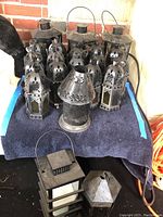 Overview of multiple metal lanterns of various designs and sizes on a towel, showing 21 pieces in total.