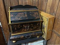 Front view of black lacquer writing trunk with gold chinoiserie scenes and separate natural wood box leaning beside it