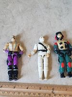 Three GI Joe action figures standing on a grey surface with ruler for scale, showing overall condition and size.