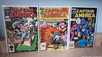 Three Captain America comic books displayed upright, showing issues #301, #308, and #315 with visible wear.