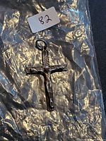 Cross pendant laid on a clear plastic surface with seller lot number 82 shown.