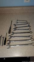 Photo showing 10 combination wrenches and 2 screwdrivers on a countertop.