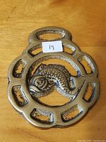 Front of vintage horse brass showing embossed fish design within horseshoe shape