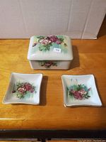 Full view of the three-piece vintage Oakcrest china set: one rectangular lidded holder and two square ashtrays, all decorated with floral patterns.