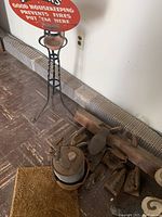 Vintage ash tray stand with red round top beside several old metal flat irons and a metal kettle.