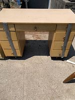 Wooden desk with six drawers on the sides and one drawer in the center, light wood finish, with metal handles for drawers.