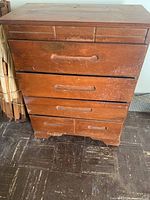 Front view of the wooden dresser showing four large drawers and three smaller drawers at top, with worn and marked surface.